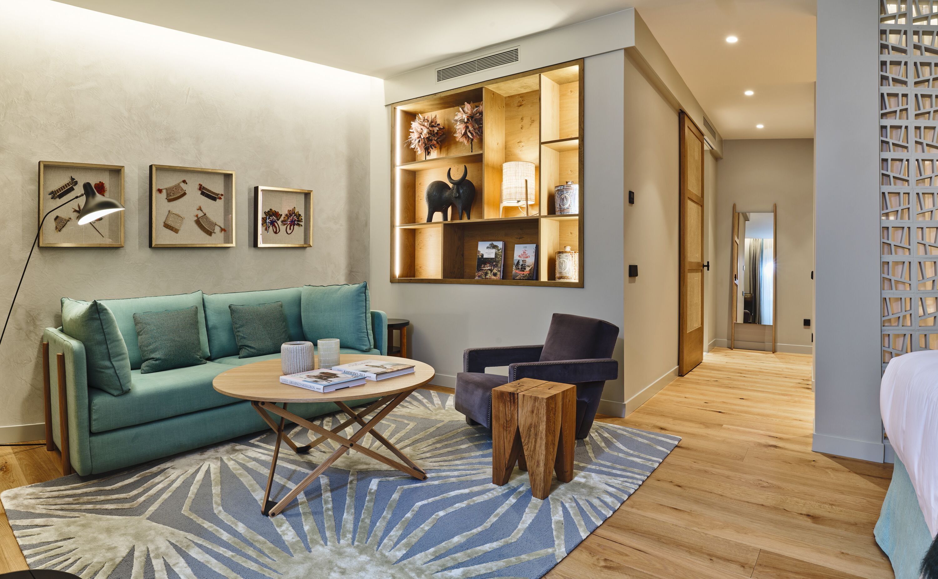 Un salon moderne avec un canapé de couleur turquoise, une table basse ronde et une table d’appoint en bois. On y trouve une bibliothèque avec des objets décoratifs et une lampe.