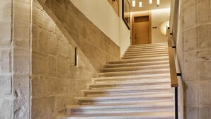 Una escalera de piedra con barandilla de madera, que sube hasta una puerta de madera.
