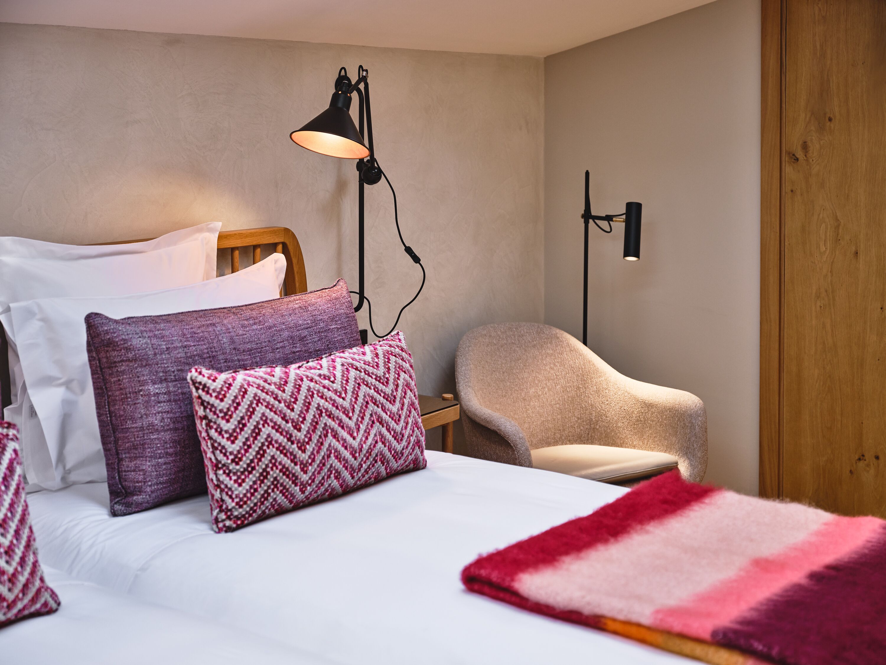 Un lit bien fait, agrémenté d’oreillers à motifs, une lampe de chevet, une chaise et une porte en bois.