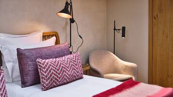 Un lit bien fait, agrémenté d’oreillers à motifs, une lampe de chevet, une chaise et une porte en bois.