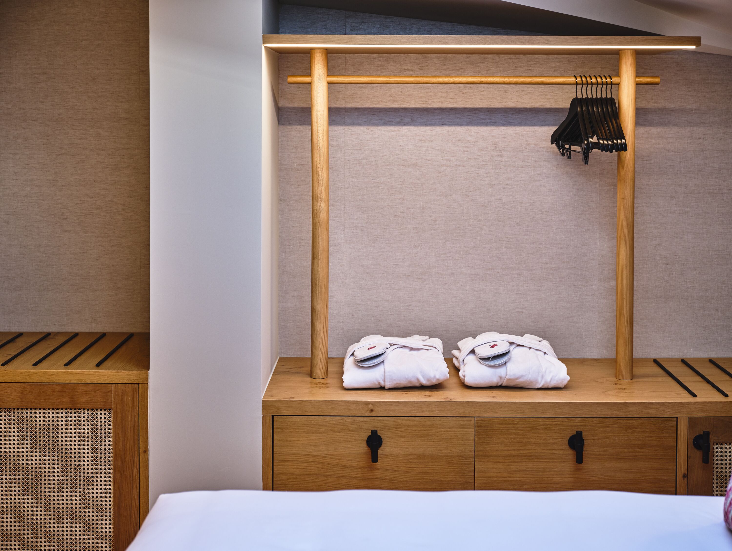 Habitación de hotel con tocador de madera, toallero y cama con cubrecama blanco.