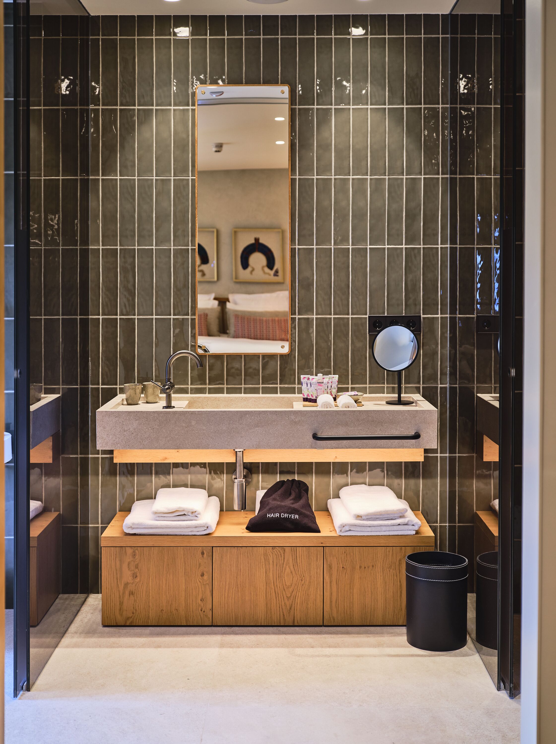 Un baño moderno con un espejo grande, un lavabo con toallero y un secador de pelo sobre una estantería de madera.