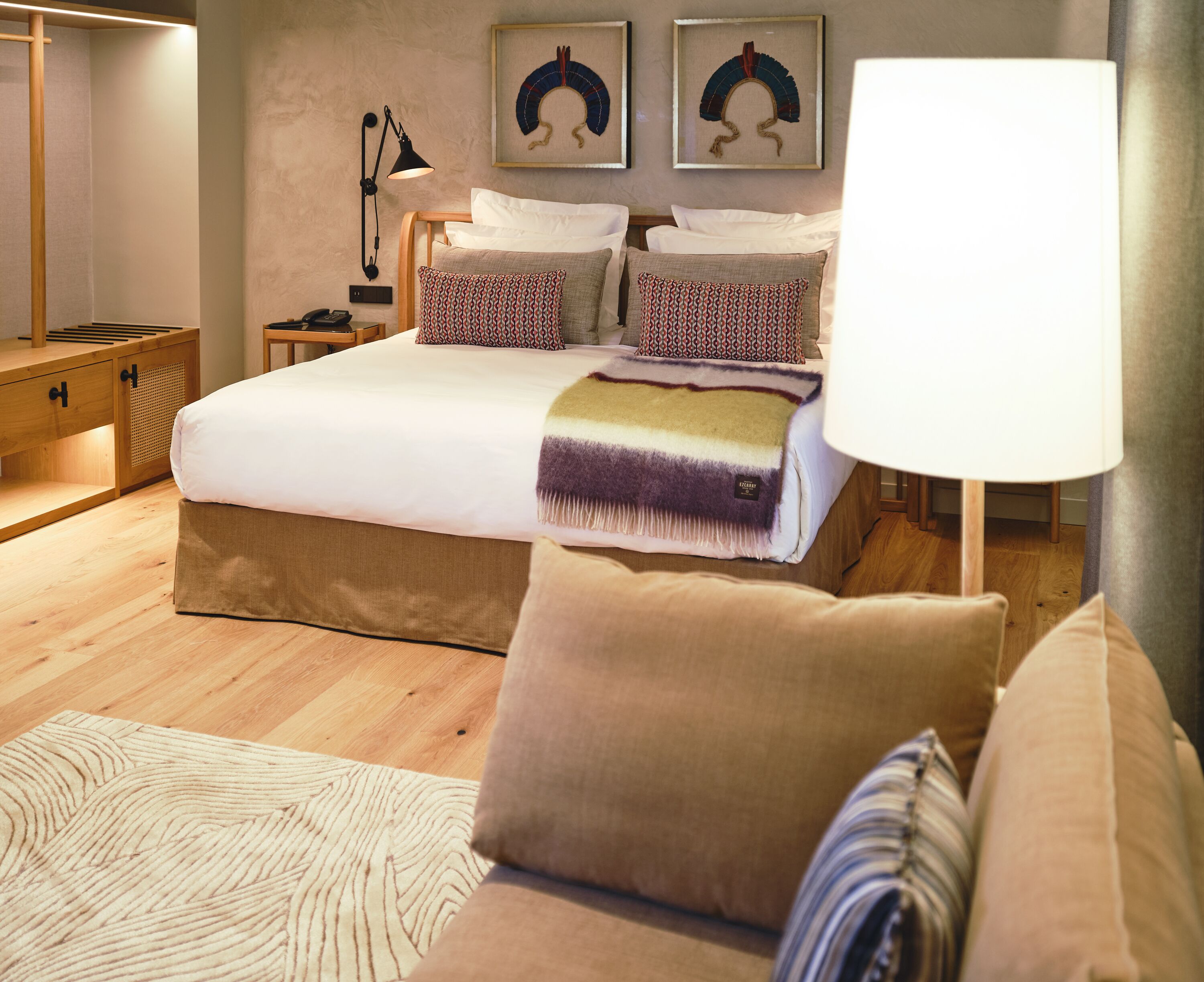 Un dormitorio con una cama grande, mesitas de noche, una lámpara de noche, una mesita de madera, un tapete estampado y un sofá.