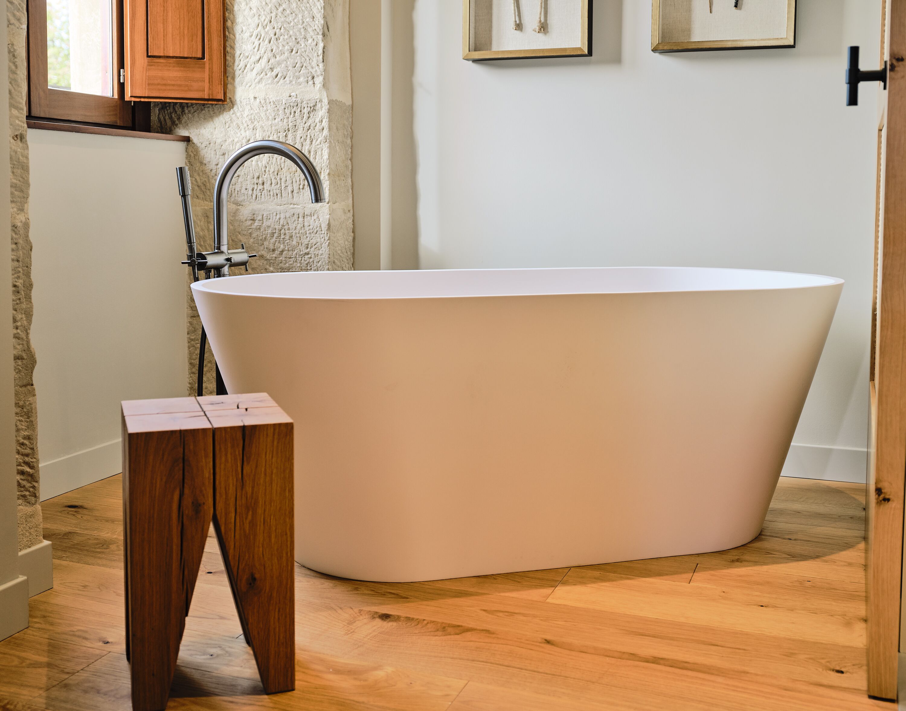 A modern bathroom with a freestanding bathtub, wooden floor, and a small wooden stool.