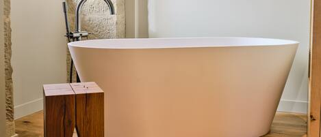 A modern bathroom with a freestanding bathtub, wooden floor, and a small wooden stool.