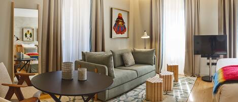 A modern hotel room with a sofa, a round table, a TV, and a lamp.