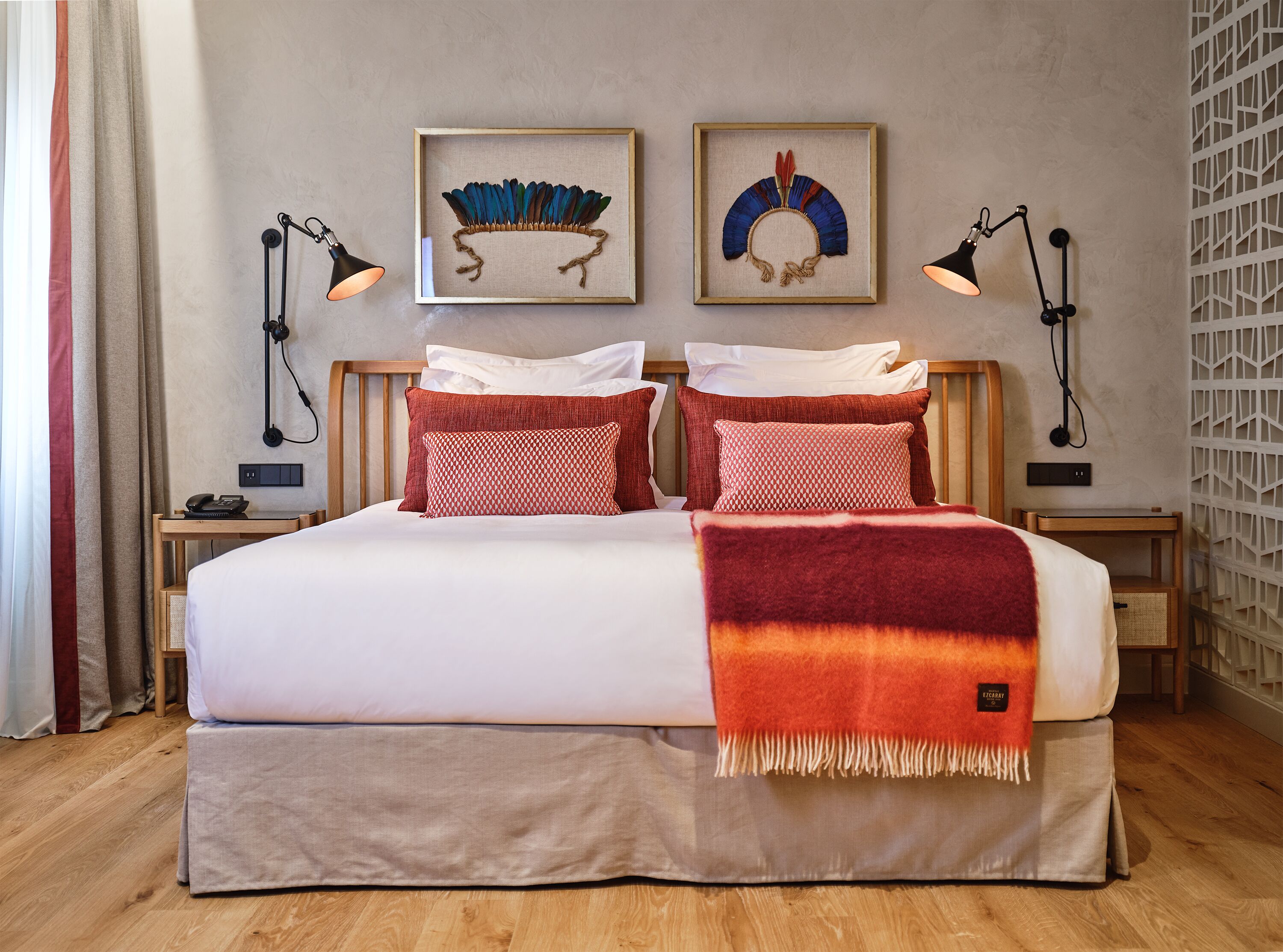 Un lit bien fait, recouvert d’une couverture blanche et rouge, avec deux oreillers et un élément décoratif fixé au mur, au niveau de la tête de lit.