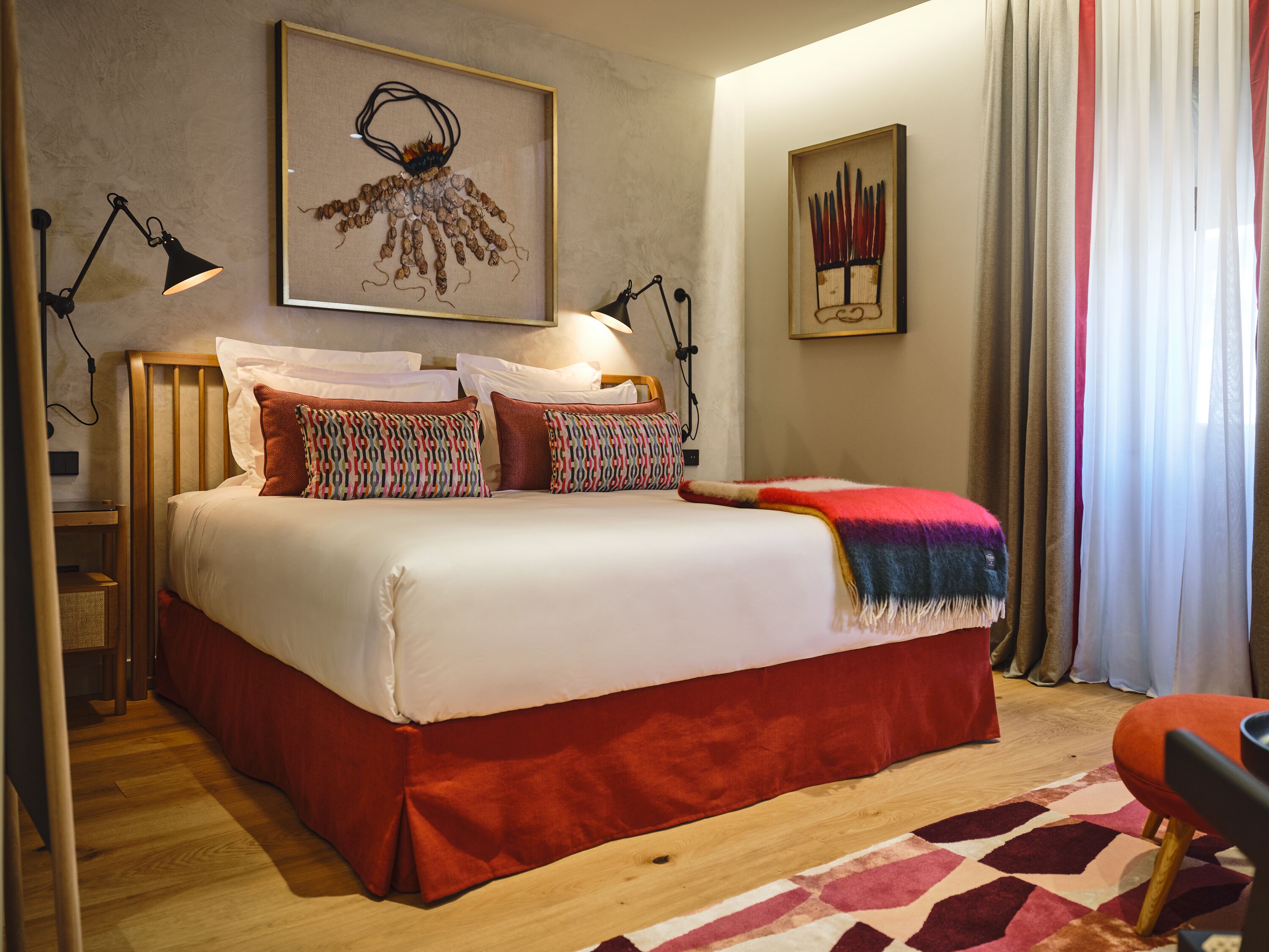 A neatly made bed with a red skirt, two bedside lamps, and a colorful pillow.