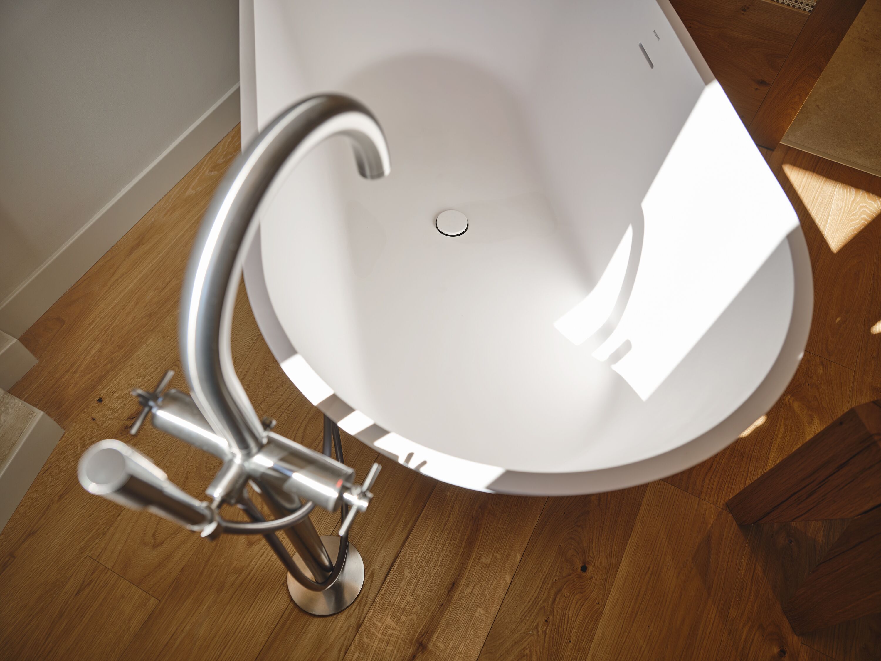 A modern bathroom with a white freestanding bathtub, a chrome faucet, and wooden flooring.