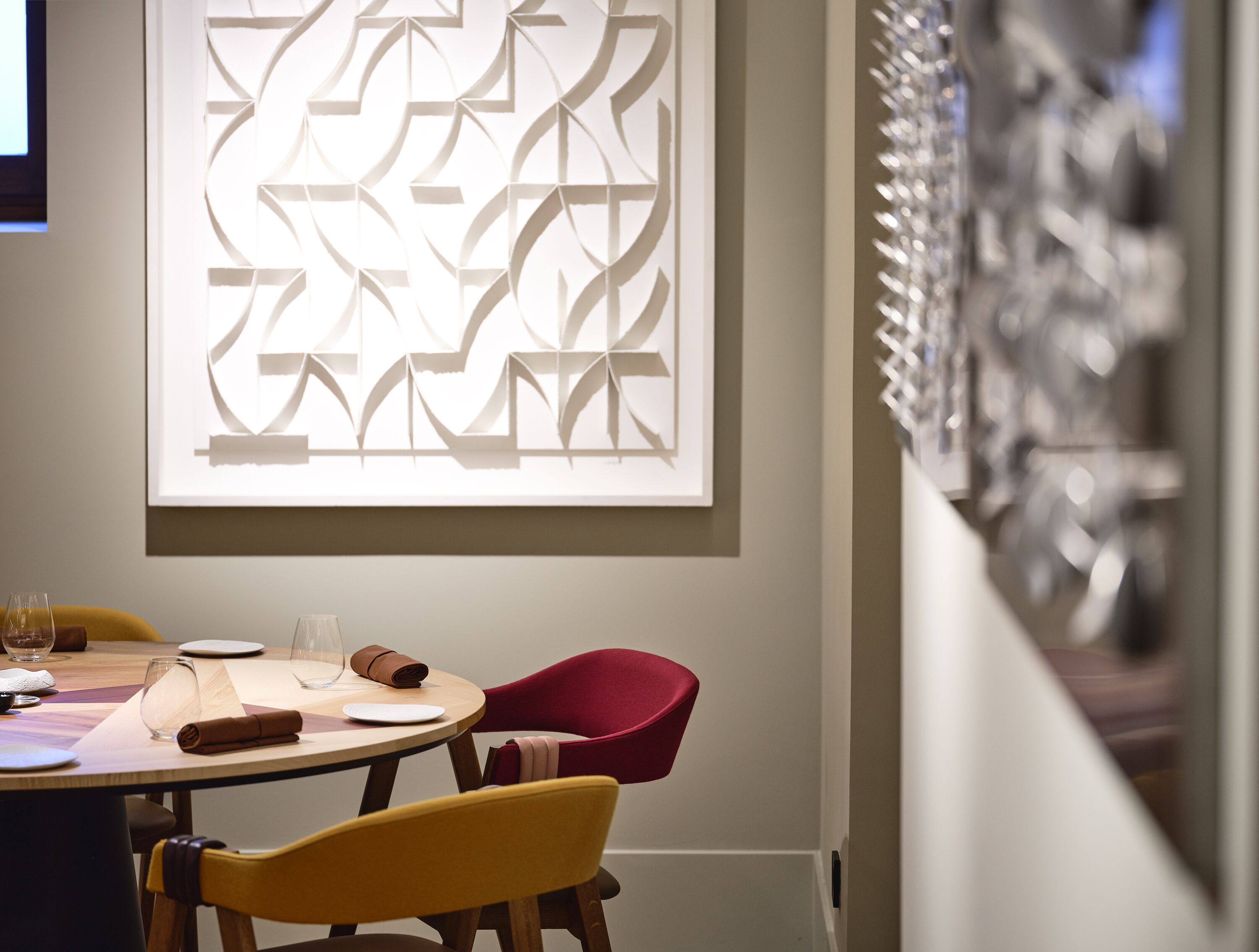 A dining area with a table set for two, featuring a modern geometric wall art piece above the table.