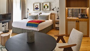 Una habitación de hotel moderna con una cama grande, una mesa redonda, una silla, un televisor y un escritorio con una lámpara y libros.