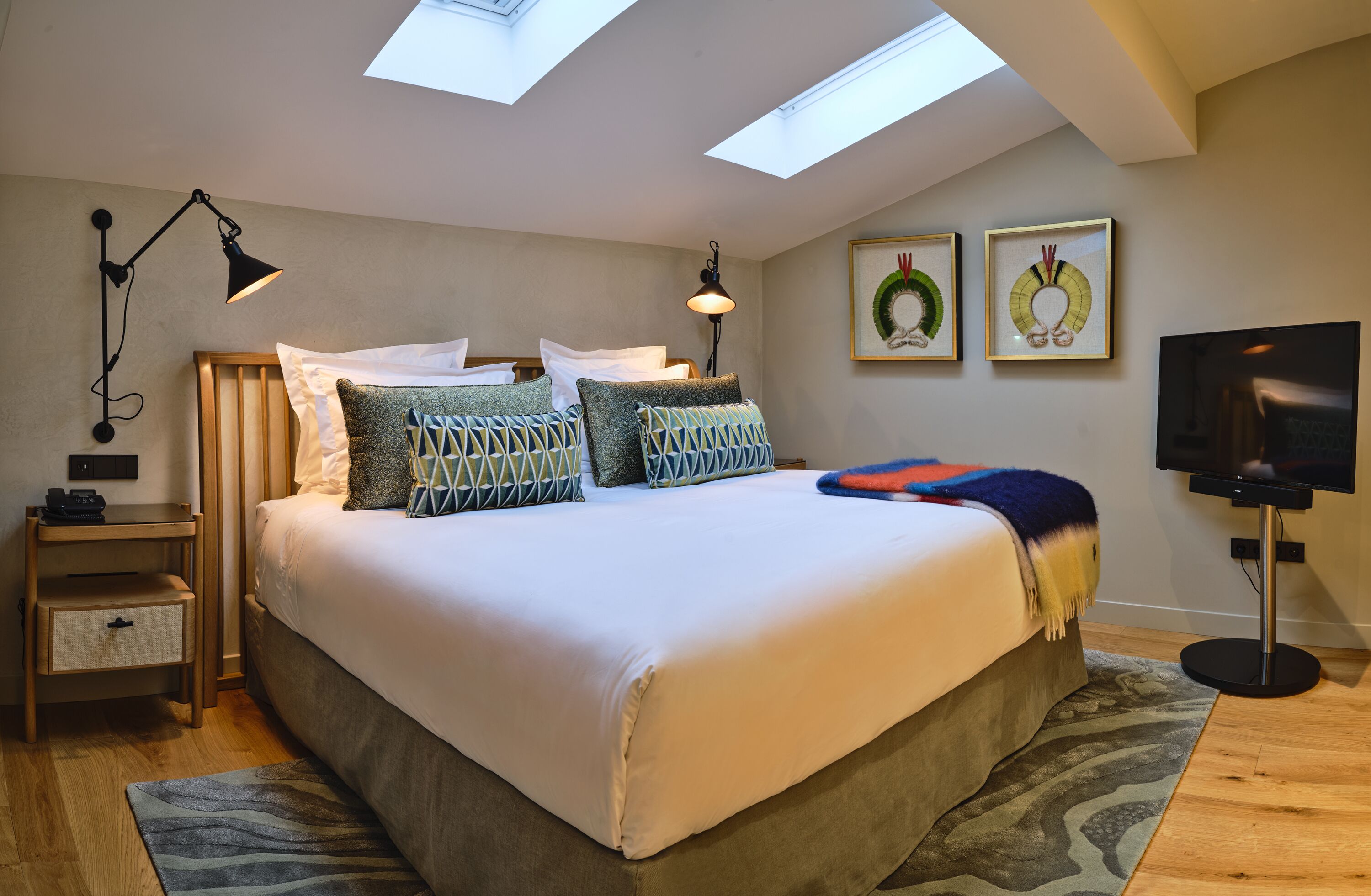 A bedroom with a large bed, skylights, a TV, and artwork on the wall.