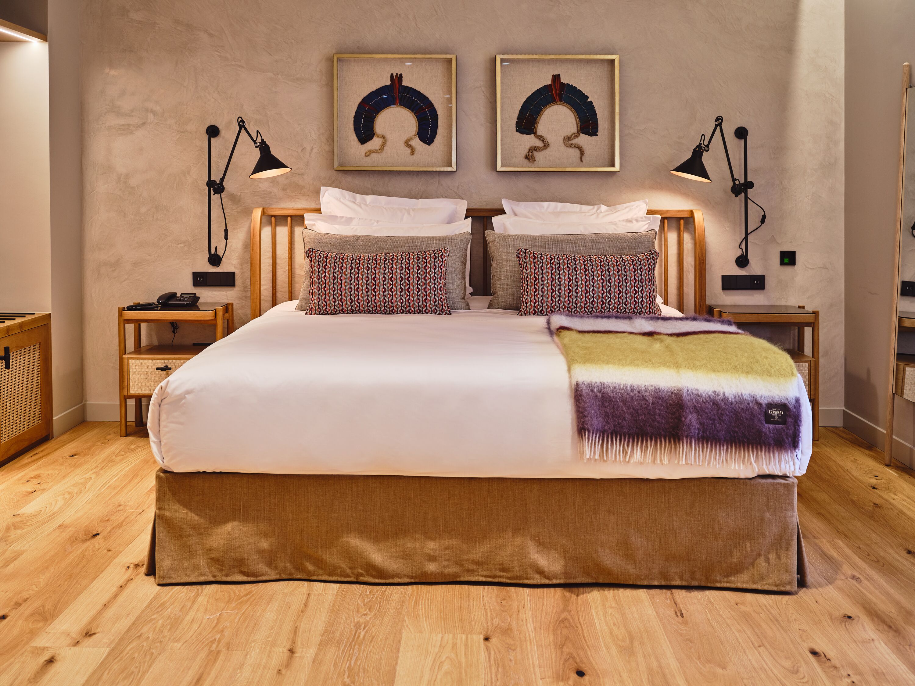 Un dormitorio ordenado con una cama grande, dos mesitas de noche y dos lámparas de pared.