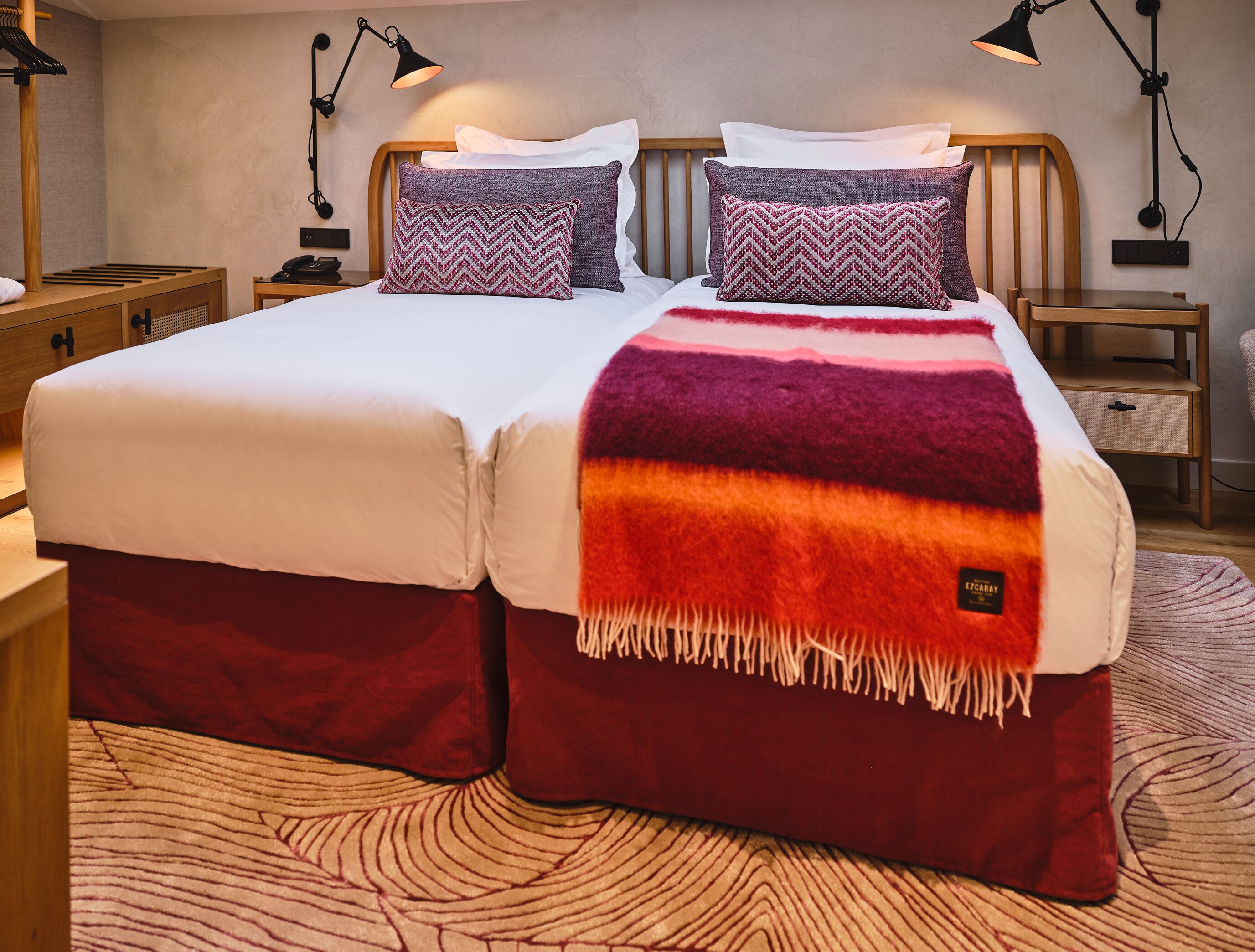 A double bed with a red and orange blanket, two pillows, and two bedside lamps.