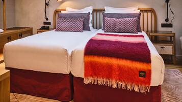 A double bed with a red and orange blanket, two pillows, and two bedside lamps.