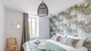 Un dormitorio con una cama, una silla, un ventanal y una pared con un diseño de hojas.