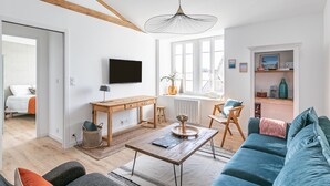 Una sala de estar moderna con techo de madera, un ventanal grande, un televisor montado en la pared, un sofá, una mesa de centro y un escritorio con una silla.