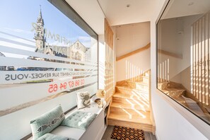 A modern interior with a view of a church through a window, a staircase, and a seating area with cushions. - Sieck - Joli Appartement Vue mer (Carantec)
