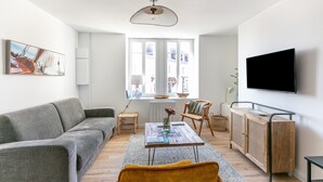 A modern living room with a grey sofa, a yellow armchair, a wooden coffee table, and a TV mounted on the wall.