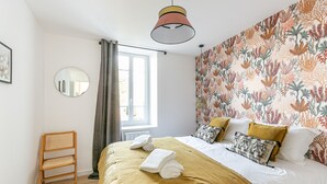 A bedroom with a bed, a chair, a window, and a mirror.