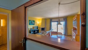 Une cuisine dotée d’un plan de travail en bois, un coin repas avec des chaises, une cheminée et une vue sur le salon.
