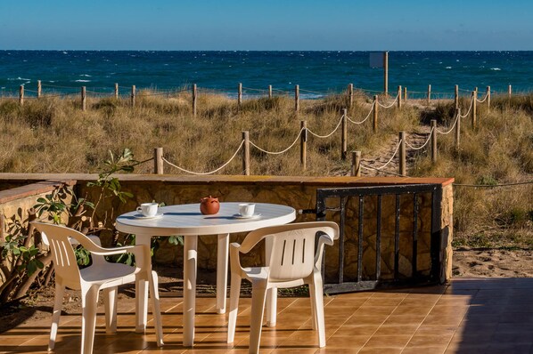 A round table with two chairs and a teapot, set against a coastal backdrop with a view of the sea.