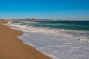 A beach with waves, a clear sky, and distant buildings.