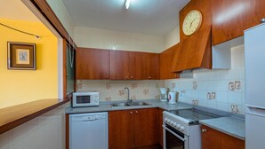 Une cuisine avec des meubles de rangement en bois, un four à micro-ondes, un lave-vaisselle, un four et une horloge au mur.