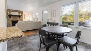 A modern kitchen with a granite countertop, a round dining table with four chairs, a stone fireplace, and large windows offering a view of the outdoors. - 4BR Home Minutes to DOWNTOWN, RAD & BILTMORE (Arden)