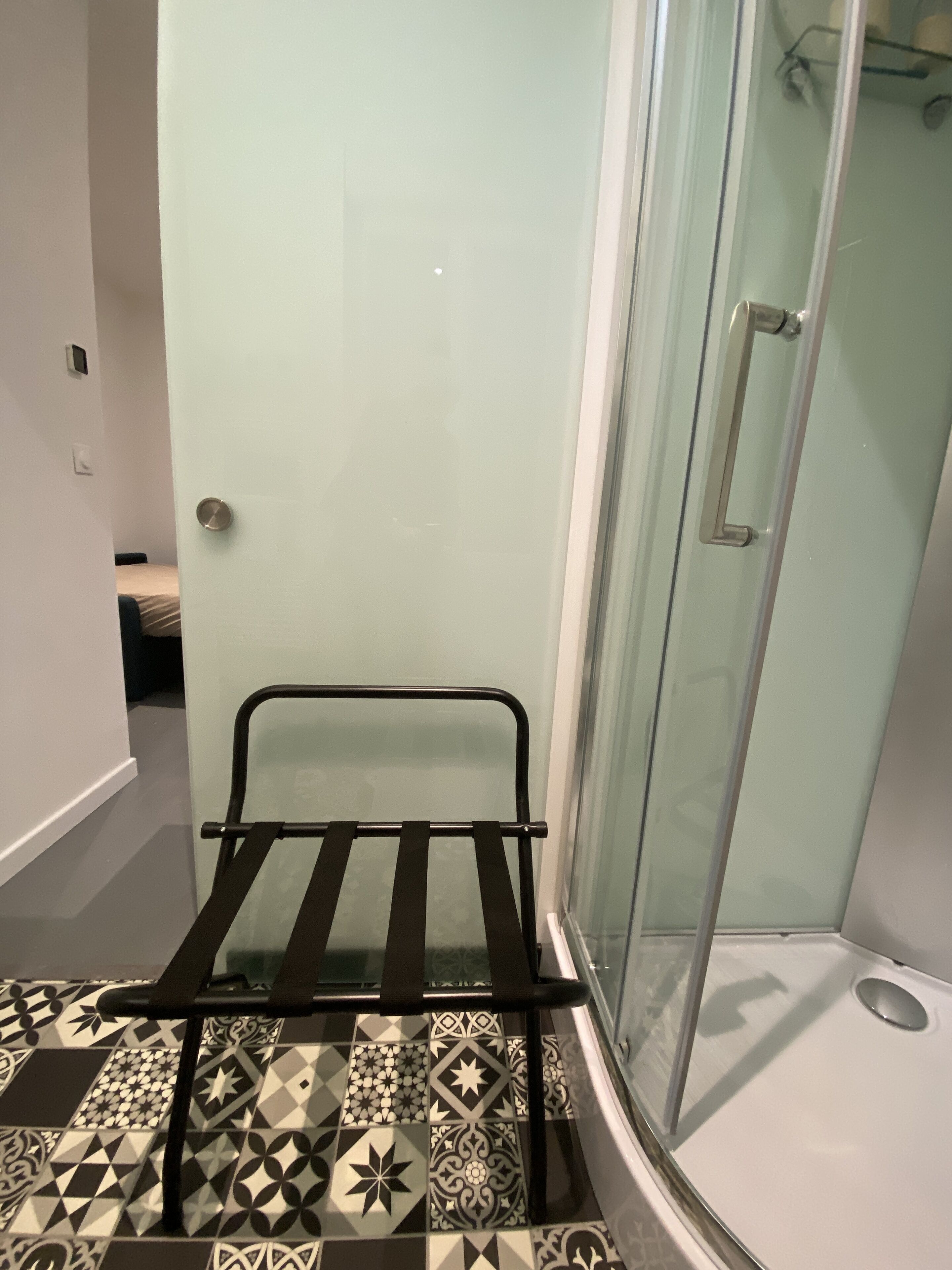 A bathroom with a shower, a towel rack, and patterned floor tiles.