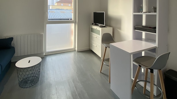 A modern, minimalistic living room with a sofa, a small round table, a TV, and a white desk with a chair. - #Casamara 1 2-bed apartment | Netflix (Amiens)
