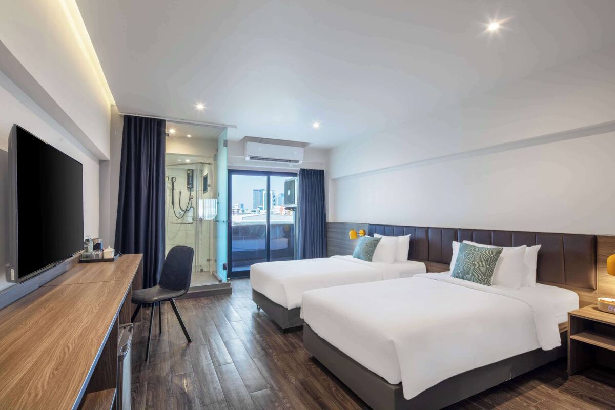 A hotel room with two beds, a desk, a TV, and a view of the city.