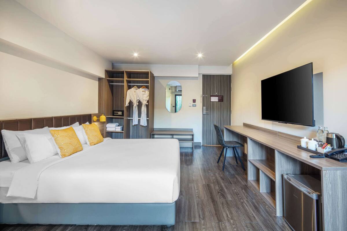 A modern hotel room with a large bed, a desk, a television, and a wardrobe.
