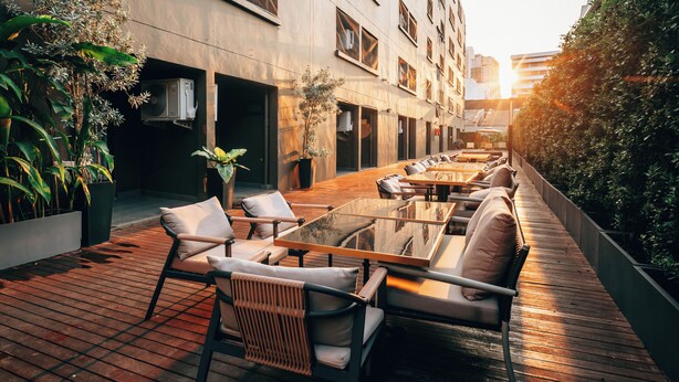 Een terras met tafels en stoelen, omringd door potplanten en een gebouw met veel ramen.