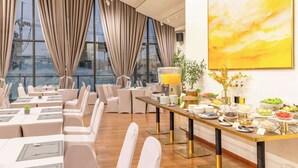 Een eetgedeelte met tafels gedekt voor een maaltijd, een buffet met diverse gerechten, en een groot raam met gordijnen.