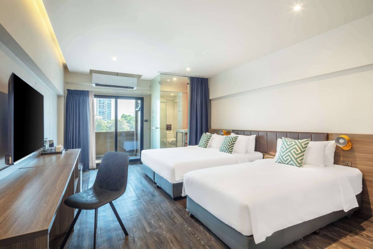 A hotel room with two beds, a desk, a chair, and a TV.