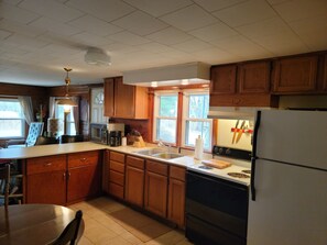 Una cocina con armarios de madera, un refrigerador, una estufa, un lavamanos y un comedor con una silla y mesa.
