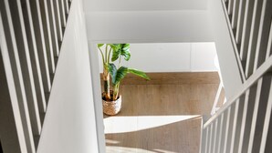 A modern staircase with white railings and a wooden floor leading to a landing. A potted plant is visible on the landing. - Superb T3 Duplex, lagoon-side (Collectivité de Saint-Martin)