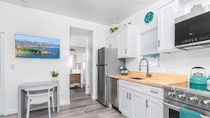 A modern kitchen with white cabinets, a stainless steel refrigerator, a stove, and a sink. - 30+ Night | Stylish Studio w/ Sun Deck | Private Yet Central to the Newport Favorites! (Newport Beach)