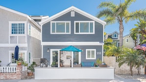 A two-story house with a balcony, a grill, and a patio area with outdoor furniture. - 30+ Night | Stylish Studio w/ Sun Deck | Private Yet Central to the Newport Favorites! (Newport Beach)