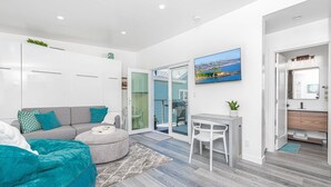 A modern living room with a grey sofa, teal pouf, and a small round table. - 30+ Night | Stylish Studio w/ Sun Deck | Private Yet Central to the Newport Favorites! (Newport Beach)