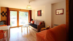 Una sala de estar acogedora con un sofá, una mesa de comedor y una silla. Hay un ventanal con cortinas, un cuadro en la pared y una lámpara de techo.