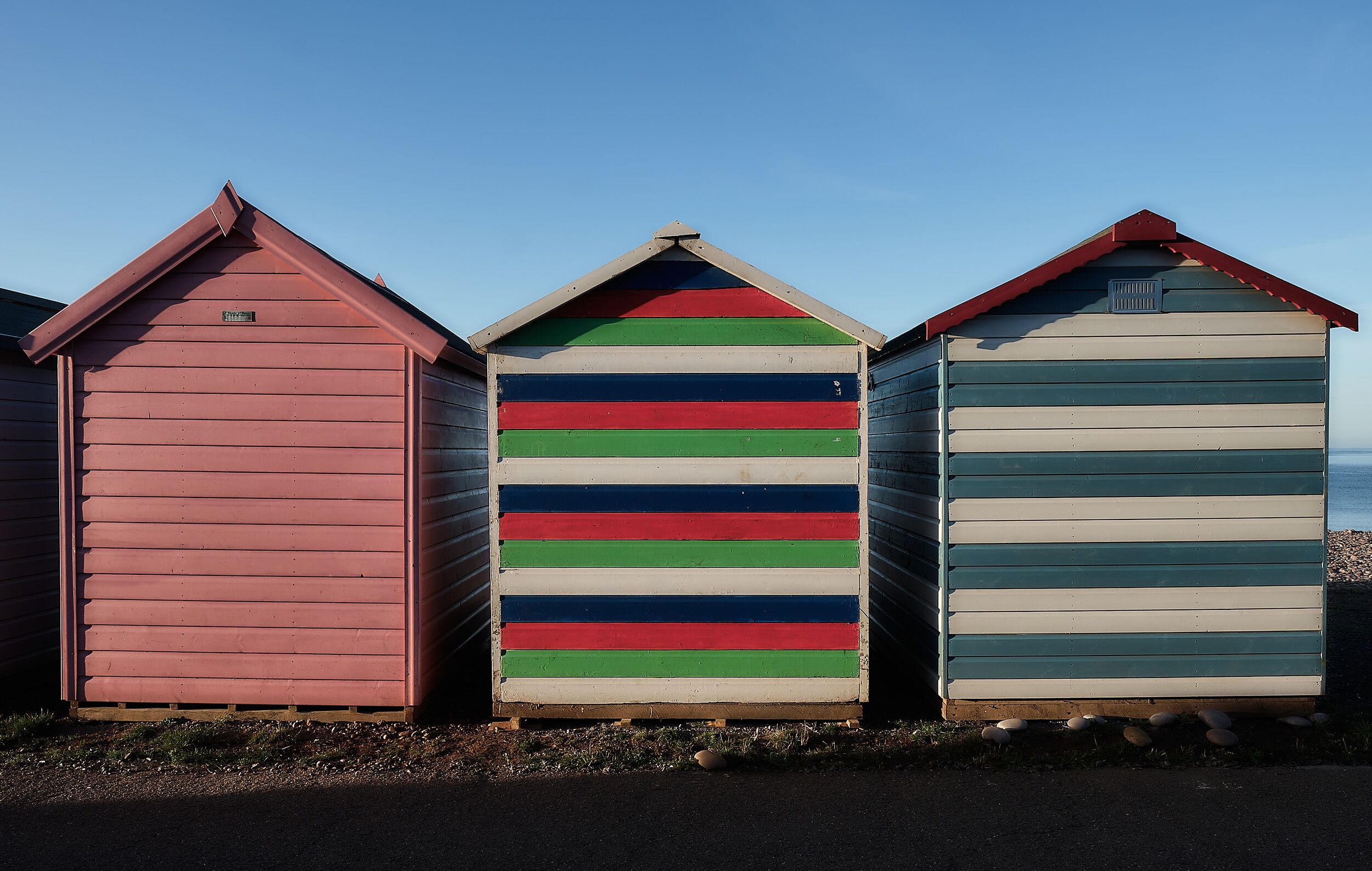 Trois cabanes de plage aux motifs rayés, avec un ciel dégagé en arrière-plan.