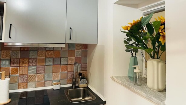 Eine Küche mit weißen Schränken, einer gefliesten Spritzschutzleiste, einem Spülbecken und einem Fenster mit einer Vase Sonnenblumen.