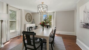 A dining room with a long table, chairs, a chandelier, a vase with flowers, and a painting on the wall. - NEW! Historic Townhome - Live among the Mansions 3BR (Newport)