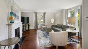 A modern living room with a fireplace, a television, a sofa, a coffee table, and a lamp. - NEW! Historic Townhome - Live among the Mansions 3BR (Newport)