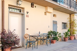 En bygning med facade, dør, balkon, et bord med stole og plantekasser.