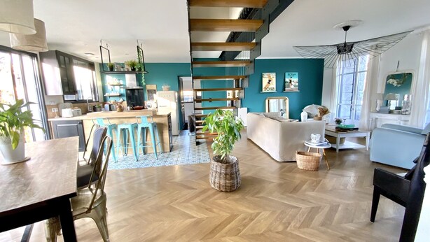 Ein modernes Interieur mit Küche, Essbereich und Wohnbereich, mit Holzböden, einem Fischgrätmuster und einer zentral platzierten Pflanze.