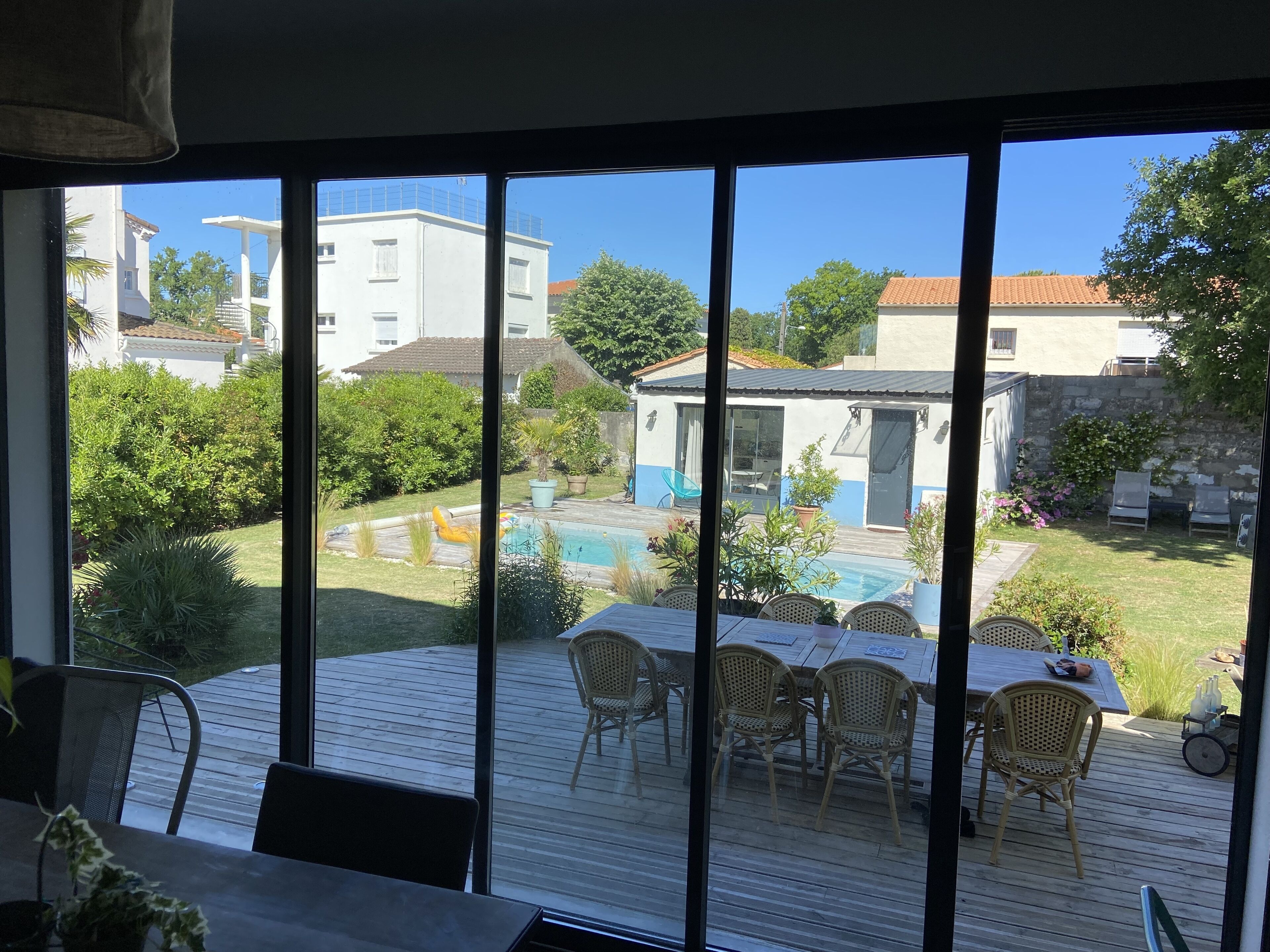 Vista desde una habitación con ventanas amplias que dan a una zona de piscina con mobiliario exterior y un pequeño edificio.