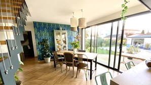 Ein Essbereich mit einem Holztisch und -stühlen, einem Bücherregal und großen Fenstern mit Blick ins Freie.